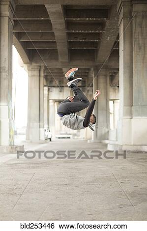 Stock Photograph - Mixed Race man jumping upside-down under bridge. Fotosearch