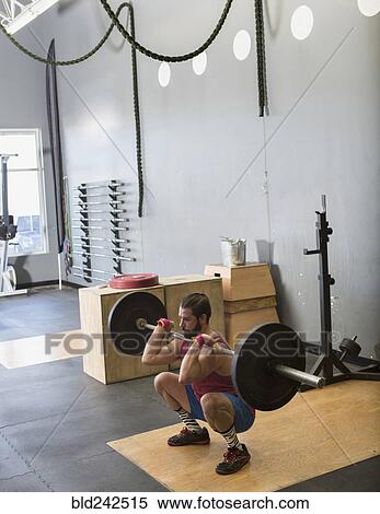 Stock Photography - Mixed Race man lifting barbell in gymnasium. Fotosearch