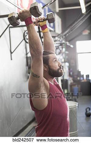 Stock Photo - Mixed Race man lifting dumbbells in gymnasium. Fotosearch