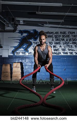 Stock Photo - Mixed Race man lifting heavy ropes in gymnasium. Fotosearch