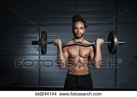 Picture - Mixed Race man lifting weights in gymnasium. Fotosearch