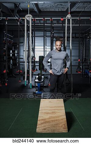 Stock Image - Mixed Race man looking at wooden platform in gymnasium. Fotosearch