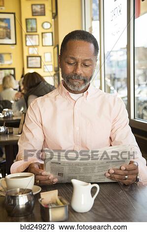 Stock Photo - Mixed Race man reading newspaper in coffee shop. Fotosearch