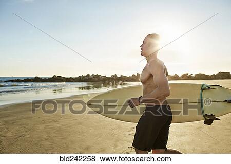 Stock Photo - Mixed race man running with surfboard on beach. Fotosearch