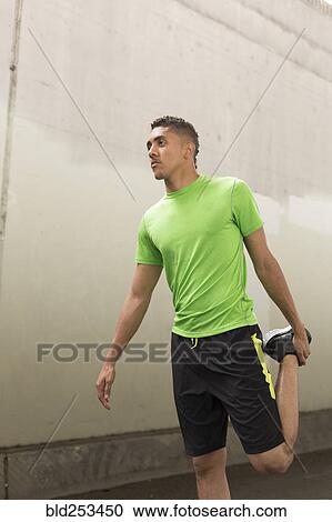Stock Image - Mixed Race man stretching leg near wall. Fotosearch