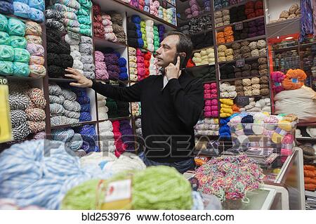 Stock Photograph - Mixed Race man talking on cell phone at yarn store. Fotosearch