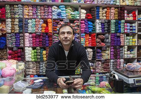 Stock Photo - Mixed Race man texting on cell phone at yarn store. Fotosearch