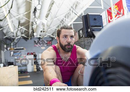Stock Image - Mixed Race man using rowing machine in gymnasium. Fotosearch
