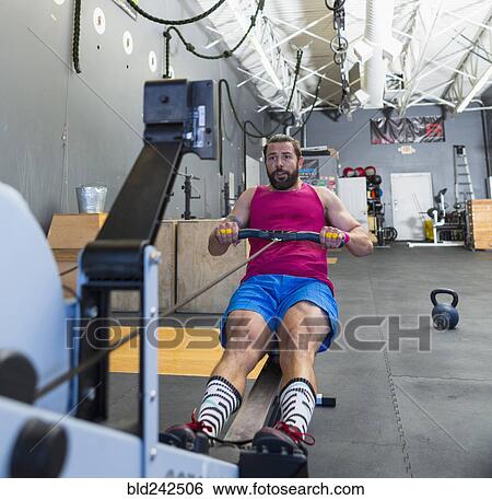 Stock Photograph - Mixed Race man using rowing machine in gymnasium. Fotosearch