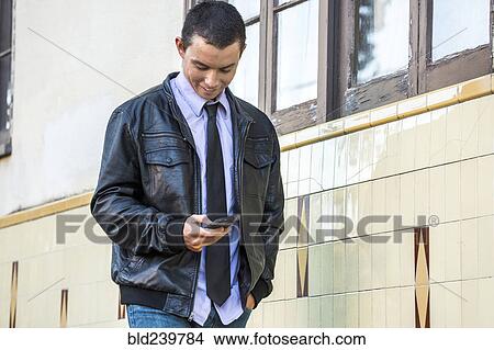 Mixed Race man wearing leather jacket texting on cell phone View Large Photo Image Picture - Mixed Race man wearing leather jacket texting on cell phone. Fotosearch