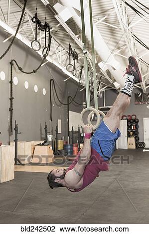 Stock Image - Mixed Race man working out with rings in gymnasium. Fotosearch