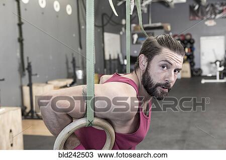 Stock Image - Mixed Race man working out with rings in gymnasium. Fotosearch