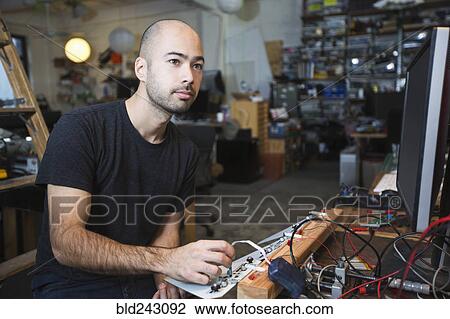 Stock Image - Mixed Race man working with electronics in workshop. Fotosearch
