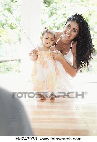 Stock Photo - Mixed Race mother kneeling on floor helping baby daughter walking. Fotosearch