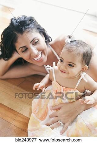 Stock Photo - Mixed Race mother laying on floor holding baby daughter. Fotosearch
