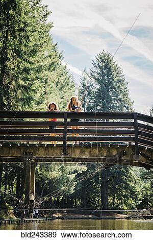 Mixed Race sisters fishing on bridge over river View Large Photo Image Stock Photo - Mixed Race sisters fishing on bridge over river. Fotosearch