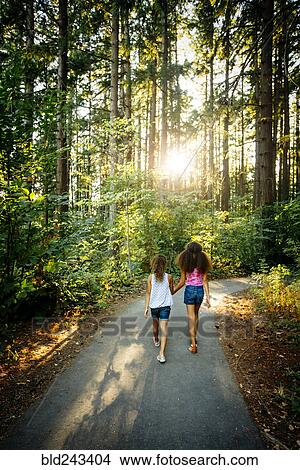 Mixed Race sisters holding hands walking on forest path View Large Photo Image Picture - Mixed Race sisters holding hands walking on forest path. Fotosearch
