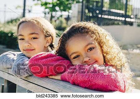 Stock Photography - Mixed Race sisters leaning on wooden railing. Fotosearch
