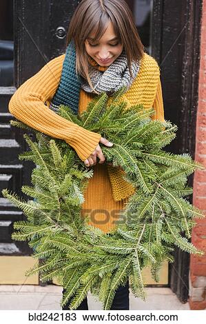 Stock Image - Mixed Race woman carrying pine wreath outdoors. Fotosearch