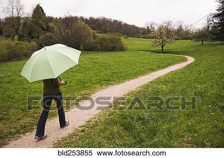 Stock Photography - Mixed Race woman carrying umbrella on path. Fotosearch