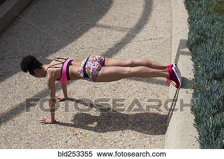 Stock Photography - Mixed Race woman doing push-ups on path curb. Fotosearch