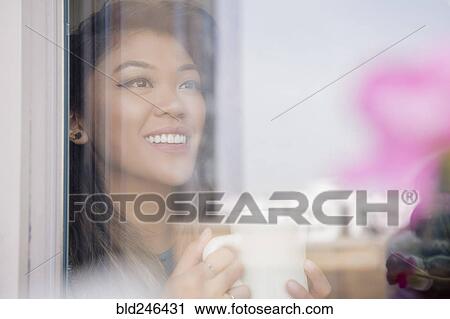 Stock Image - Mixed Race woman drinking coffee behind window. Fotosearch