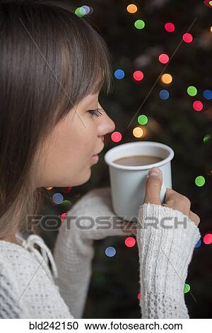 Stock Image - Mixed Race woman drinking coffee near Christmas tree. Fotosearch