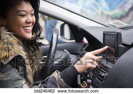Stock Image - Mixed Race woman driving car pressing touch screen. Fotosearch