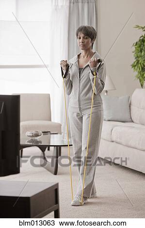 Stock Image - Mixed race woman exercising in living room. Fotosearch