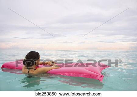 Stock Image - Mixed Race woman floating in ocean on inflatable raft. Fotosearch
