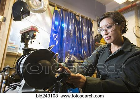 Stock Image - Mixed Race woman grinding metal rod in workshop. Fotosearch