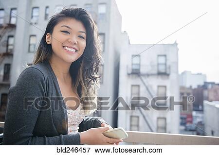Stock Photo - Mixed Race woman holding cell phone in city. Fotosearch