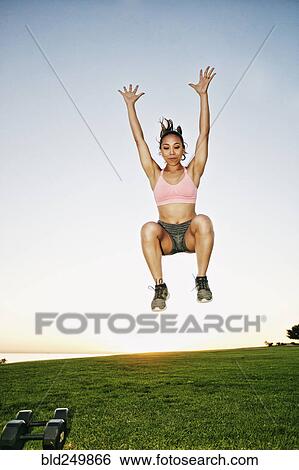 Stock Photograph - Mixed Race woman jumping in sunny field. Fotosearch
