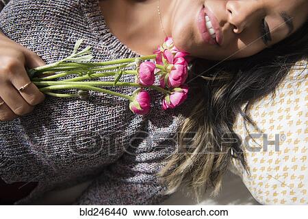 Stock Image - Mixed Race woman laying on bed holding flowers. Fotosearch