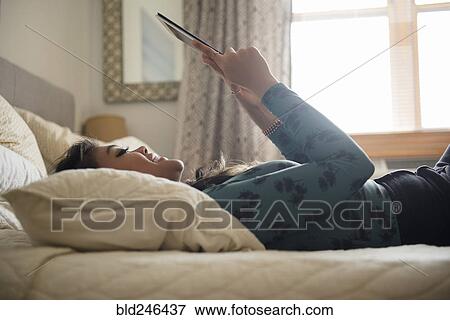 Stock Photo - Mixed Race woman laying on bed using digital tablet. Fotosearch
