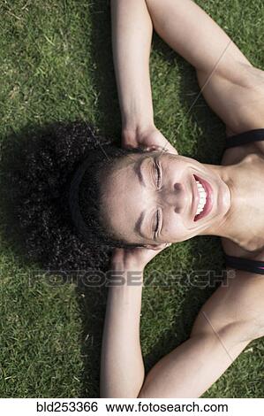 Stock Photograph - Mixed Race woman laying on grass relaxing,. Fotosearch