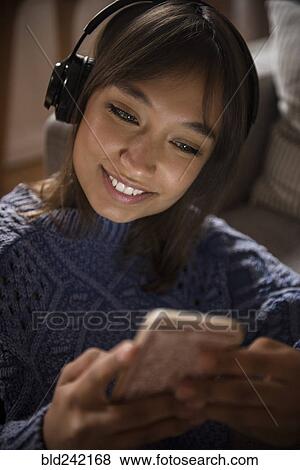 Mixed Race woman listening to cell phone with headphones View Large Photo Image Stock Photo - Mixed Race woman listening to cell phone with headphones. Fotosearch