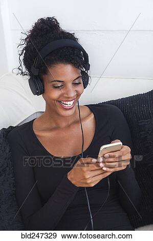 Stock Photo - Mixed Race woman listening to cell phone with headphones. Fotosearch
