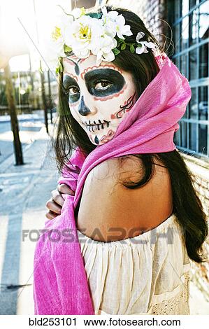 Stock Image - Mixed Race woman on sidewalk wearing scarf and skull face paint. Fotosearch