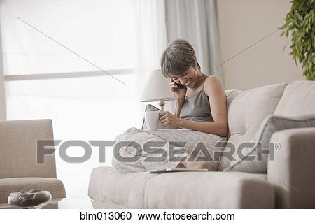 Stock Image - Mixed race woman on sofa talking on cell phone. Fotosearch