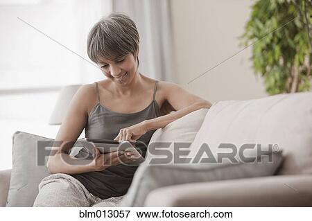 Mixed race woman on sofa using digital tablet View Large Photo Image Stock Photo - Mixed race woman on sofa using digital tablet. Fotosearch