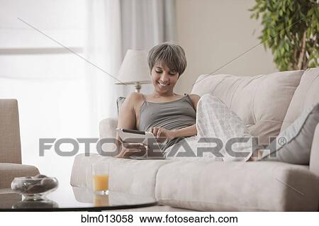Stock Photo - Mixed race woman on sofa using digital tablet. Fotosearch