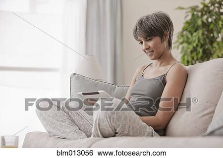 Stock Photograph - Mixed race woman on sofa using digital tablet. Fotosearch