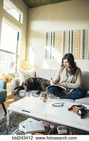 Mixed Race woman on sofa with dog writing in journal View Large Photo Image Stock Image - Mixed Race woman on sofa with dog writing in journal. Fotosearch