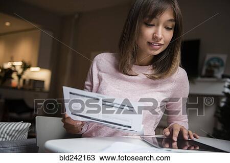 Stock Image - Mixed Race woman paying bills on digital tablet. Fotosearch