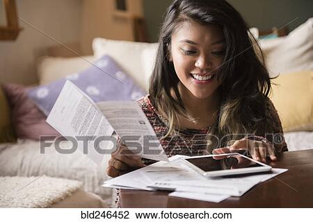 Stock Image - Mixed Race woman paying bills using digital tablet. Fotosearch