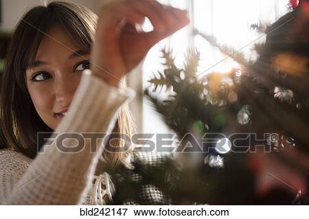 Stock Photo - Mixed Race woman placing tinsel on Christmas tree. Fotosearch