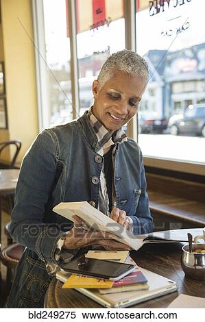 Stock Photography - Mixed Race woman reading travel guidebook in coffee shop. Fotosearch