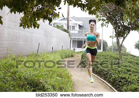 Stock Image - Mixed Race woman running on path in park. Fotosearch