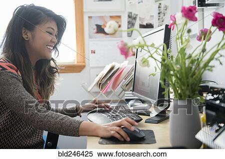 Stock Photography - Mixed Race woman sitting at desk using computer. Fotosearch